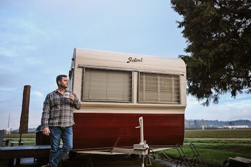 Man with mug standing by a vintage camper trailer